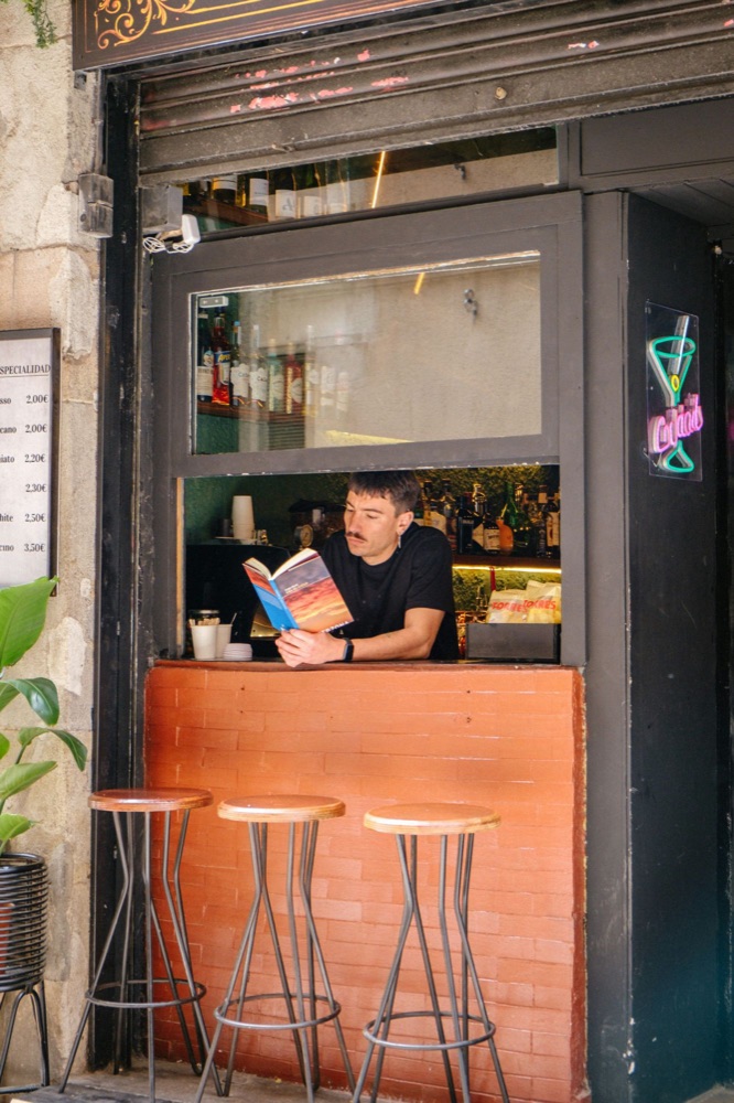A barista leaning out of a small bar window, reading