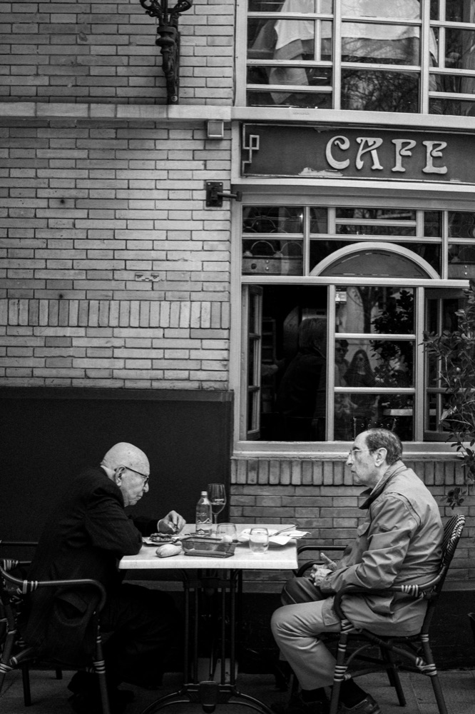 Two older men talking at an outdoor café table